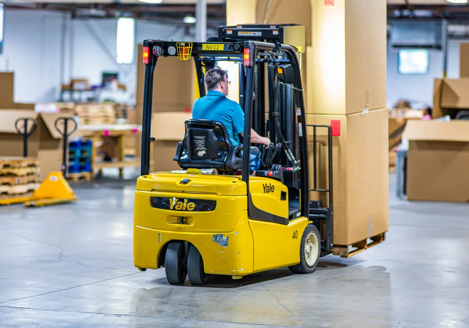 Forklift carrying palletized cartons across the open warehouse floor