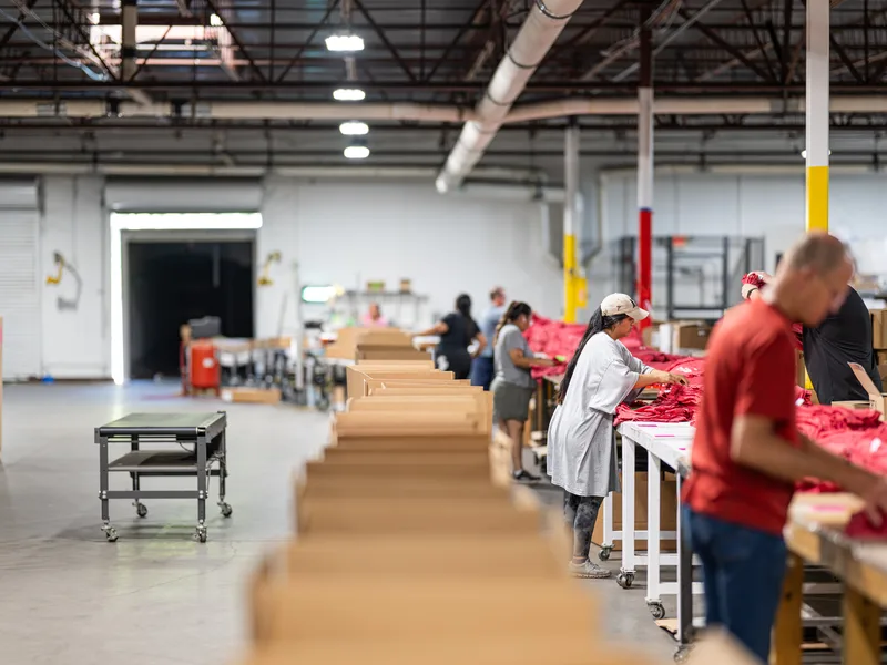 Apparel kitting line — team packing folded shirts into cartons
